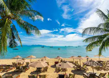 Beautiful tropical beach sea and ocean with coconut palm tree  and umbrella and chair on blue sky and white cloud for holiday vacation travel