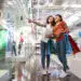Two smiling black beautiful girls looking at shop window, holding bags and standing in shopping mall. One girl is pointing at something.
