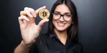 young successful confident woman with glasses holds a gold bitcoin in her hand