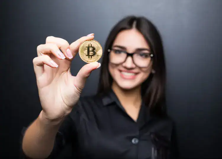 young successful confident woman with glasses holds a gold bitcoin in her hand