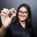 young successful confident woman with glasses holds a gold bitcoin in her hand