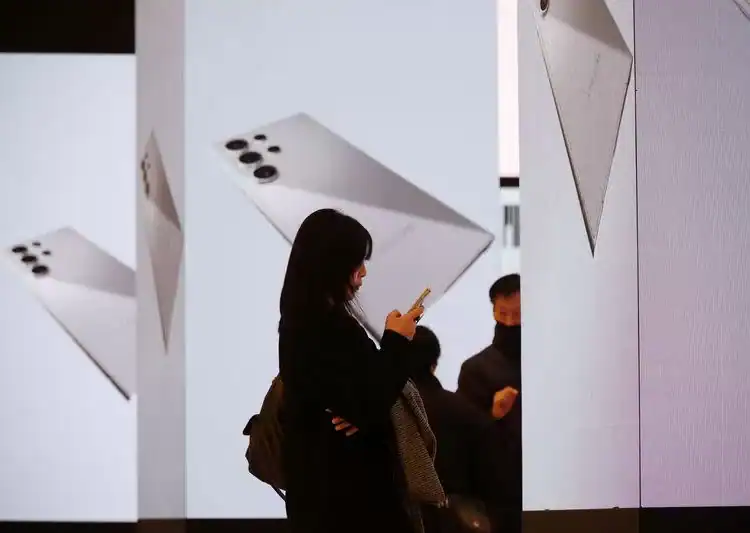 Una mujer utiliza su teléfono móvil delante de unos paneles electrónicos que promocionan los nuevos smartphones insignia de Samsung Electronics, la serie Galaxy S24, en Seúl, Corea del Sur · Reuters
