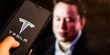 In this photo illustration the Tesla logo, US leading EV cars producer, is shown on a mobile phone screen against the Elon Musk portrait displayed on a computer screen as Tesla sales drop in worldwide as Elon Musk, the owner of Tesla, backs far right politicians -February 9, 2025. (Photo by Dominika Zarzycka/NurPhoto via Getty Images)