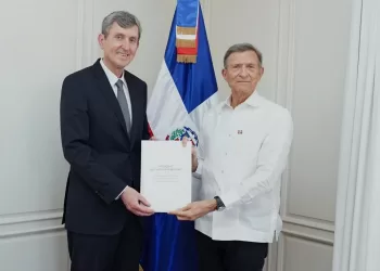 El embajador de Rusia entrega sus cartas credenciales al canciller de República Dominicana, con la bandera dominicana al fondo.