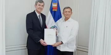 El embajador de Rusia entrega sus cartas credenciales al canciller de República Dominicana, con la bandera dominicana al fondo.