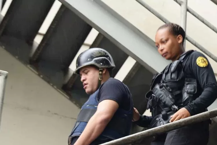 Oficial de la Policía Nacional escolta a Mantequilla con casco y chaleco antibalas por una escalera metálica en un operativo de seguridad.