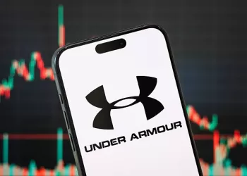 CHONGQING, CHINA - MAY 11: In this photo illustration, the logo of Under Armour, Inc. is displayed on a smartphone screen, with the company's latest stock market chart in the background, reflecting investor sentiment and recent trading activity, on May 11, 2025, in Chongqing, China. Under Armour is an American sportswear and athletic performance apparel company known for its innovative moisture-wicking fabrics and high-performance gear. (Photo illustration by Cheng Xin/Getty Images)