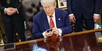 US President Donald Trump holds an Apple Inc. iPhone during an executive order signing in the Oval Office of the White House in Washington, DC, US, on Friday, May 23, 2025. Trump on Friday signed orders meant to accelerate the construction of nuclear power plants, including small, untested designs that offer the promise of rapid deployment but have yet to be built in the US. Photographer: Samuel Corum/Sipa/Bloomberg via Getty Images