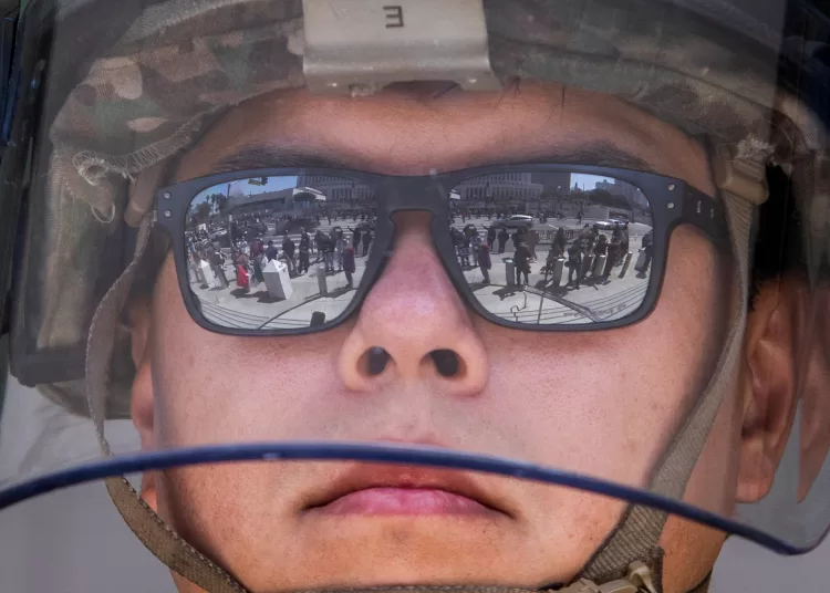 Demonstrators are reflected in the glasses of a California National Guard member standing guard outside the Federal Building during a protest in response to federal immigration operations in Los Angeles, on June 9, 2025. US President Donald Trump on June 9 ordered active-duty Marines into Los Angeles, vowing those protesting immigration arrests would be "hit harder" than ever. Protests in Los Angeles, home to a large Latino population, broke out on June 6, triggered by immigration raids that resulted in dozens of arrests of what authorities say are illegal migrants and gang members. (Photo by Apu GOMES / AFP)