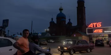 People on a motorcycle and cars drive in front of a church and a supermarket in the town of Lozova, in the Kharkiv region, on July 17, 2025, amid the Russian invasion of Ukraine. (Photo by Roman PILIPEY / AFP)