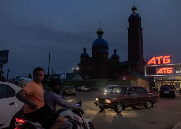 People on a motorcycle and cars drive in front of a church and a supermarket in the town of Lozova, in the Kharkiv region, on July 17, 2025, amid the Russian invasion of Ukraine. (Photo by Roman PILIPEY / AFP)