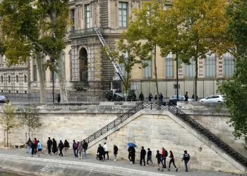Pedestrians walk on Quai Francois Mitterrand as French police officers stand next to a furniture elevator used by robbers to enter the Louvre Museum, in Paris on October 19, 2025. Robbers broke in to the Louvre and fled with jewellery on October 19, 2025 morning. France's Interior Minister said that jewellery stolen from the Louvre Museum was "priceless". The minister told French news outlets France Inter, France Info and Le Monde that "three or four" thieves had focused on two displays in the exhibition venue's "Gallerie d'Apollon" ("Apollo's Gallery"), completing their broad daylight robbery in just seven minutes. (Photo by Dimitar DILKOFF / AFP)