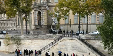 Pedestrians walk on Quai Francois Mitterrand as French police officers stand next to a furniture elevator used by robbers to enter the Louvre Museum, in Paris on October 19, 2025. Robbers broke in to the Louvre and fled with jewellery on October 19, 2025 morning. France's Interior Minister said that jewellery stolen from the Louvre Museum was "priceless". The minister told French news outlets France Inter, France Info and Le Monde that "three or four" thieves had focused on two displays in the exhibition venue's "Gallerie d'Apollon" ("Apollo's Gallery"), completing their broad daylight robbery in just seven minutes. (Photo by Dimitar DILKOFF / AFP)