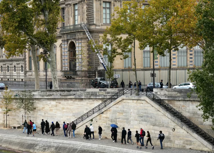 Pedestrians walk on Quai Francois Mitterrand as French police officers stand next to a furniture elevator used by robbers to enter the Louvre Museum, in Paris on October 19, 2025. Robbers broke in to the Louvre and fled with jewellery on October 19, 2025 morning. France's Interior Minister said that jewellery stolen from the Louvre Museum was "priceless". The minister told French news outlets France Inter, France Info and Le Monde that "three or four" thieves had focused on two displays in the exhibition venue's "Gallerie d'Apollon" ("Apollo's Gallery"), completing their broad daylight robbery in just seven minutes. (Photo by Dimitar DILKOFF / AFP)
