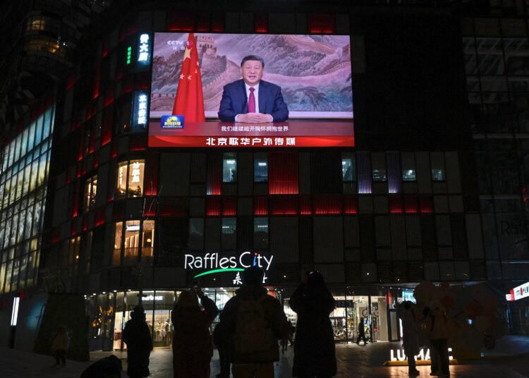 La gente está de pie bajo una gran pantalla que muestra al presidente de China, Xi Jinping, pronunciando un discurso antes de las celebraciones de Nochevieja en Beijing el 31 de diciembre de 2025. El presidente de China, Xi Jinping, dijo el 31 de diciembre que "la reunificación... es imparable" mientras se dirigía a la nación poco después de que el ejército de Beijing anunciara el fin de los simulacros de fuego vivo alrededor de Taiwán. (Foto de WANG Zhao / AFP)