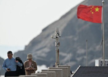 Los visitantes pasan por un poste de cámara de vigilancia (C) y una bandera china (R) en la isla de Pingtan, el punto más cercano a Taiwán, en la provincia de Fujian en el este de China el 30 de diciembre de 2025. Los ejercicios militares de China alrededor de Taiwán entraron en su segundo día el 30 de diciembre, las sextas maniobras importantes que Beijing ha celebrado cerca de la isla autogobernada en los últimos años. (Foto de ADEK BERRY / AFP vía Getty Images)