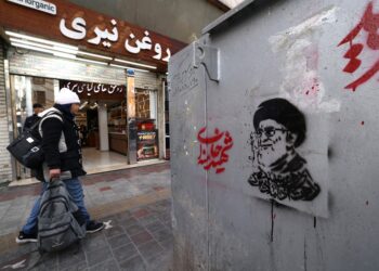 Un iraní pasa junto a una tienda y una imagen del líder supremo asesinado de Irán, el ayatolá Ali Khamenei (R), a lo largo de una calle en la plaza Tajrish en Teherán el 7 de marzo de 2026. El ejército de Irán dijo el sábado que su marina había lanzado una ola de ataques con drones dirigidos a Israel, así como a bases estadounidenses en los Emiratos Árabes Unidos y Kuwait, mientras la guerra regional hacía estragos en su segunda semana. (Foto de ATTA KENARE / AFP)