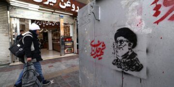 Un iraní pasa junto a una tienda y una imagen del líder supremo asesinado de Irán, el ayatolá Ali Khamenei (R), a lo largo de una calle en la plaza Tajrish en Teherán el 7 de marzo de 2026. El ejército de Irán dijo el sábado que su marina había lanzado una ola de ataques con drones dirigidos a Israel, así como a bases estadounidenses en los Emiratos Árabes Unidos y Kuwait, mientras la guerra regional hacía estragos en su segunda semana. (Foto de ATTA KENARE / AFP)