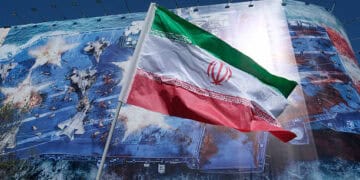 TEHERÁN, IRÁN - 1 DE MARZO: Se ve una bandera iraní contra una enorme pancarta en la esquina de la Plaza de la Revolución que representa un ataque con misiles iraní a un portaaviones estadounidense estacionado en el Golfo Pérsico durante una ceremonia de luto por el asesinato del Líder Supremo de Irán que fue asesinado en una operación conjunta llamada Epic Fury por Israel y los Estados Unidos en su residencia un día antes (28 de febrero) el 1 de marzo de 2026 en Teherán, Irán. (Foto de Kaveh Kazemi/Getty Images