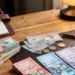 Una toma de arriba de un escritorio de madera organizado con montones ordenados de dólares estadounidenses y pesos dominicanos, una calculadora, una libreta de planificación, bolígrafos, un café y una lámpara. El enfoque está en el dinero y las herramientas de trabajo.