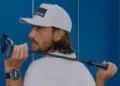alt A man wearing a white cap and shirt holds a golf club over his shoulder. He is looking back over his left shoulder. He also wears a smartwatch on his left wrist. Blue lockers are visible in the background.