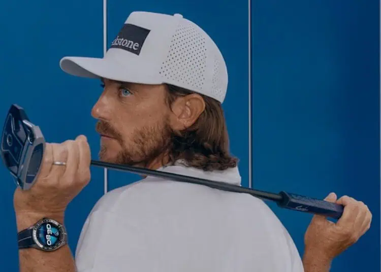 alt A man wearing a white cap and shirt holds a golf club over his shoulder. He is looking back over his left shoulder. He also wears a smartwatch on his left wrist. Blue lockers are visible in the background.