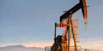 Barriles y plataforma petrolera con gráficos de precios del crudo Brent y WTI en descenso