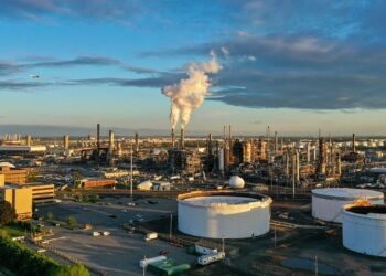 Refinería de petróleo en la costa con tanques de almacenamiento y torres de procesamiento de combustible