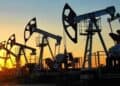 Barriles de petróleo y una plataforma de extracción de crudo con gráfico de precios al fondo