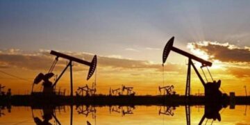 Instalación petrolera con tanques de almacenamiento y precios del crudo a la baja