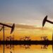 Instalación petrolera con tanques de almacenamiento y precios del crudo a la baja