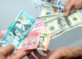 Billetes de dólares y pesos dominicanos sobre una mesa, con gráfica de tipo de cambio al fondo