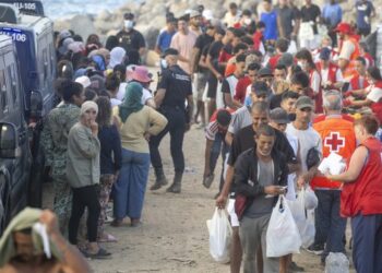Personas migrantes en la playa de El Trampolín en Ceuta, con dispositivos de atención sanitaria al fondo