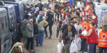 Personas migrantes en la playa de El Trampolín en Ceuta, con dispositivos de atención sanitaria al fondo