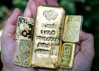 Lingotes de oro apilados sobre una superficie reflectante con el símbolo del dólar al fondo