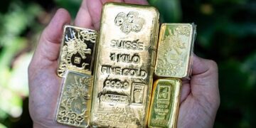 Lingotes de oro apilados sobre una superficie reflectante con el símbolo del dólar al fondo