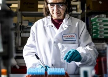 Científico sosteniendo una dosis de vacuna ARNm en laboratorio farmacéutico con equipo de investigación oncológica al fondo