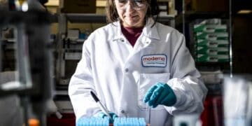 Científico sosteniendo una dosis de vacuna ARNm en laboratorio farmacéutico con equipo de investigación oncológica al fondo