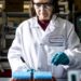 Científico sosteniendo una dosis de vacuna ARNm en laboratorio farmacéutico con equipo de investigación oncológica al fondo