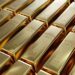 Barras de oro apiladas sobre una superficie reflectante con gráficos de precios al fondo