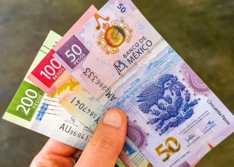 Billetes de pesos mexicanos y dólares estadounidenses sobre una mesa, con gráfica de tipo de cambio al fondo