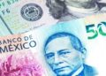 Billetes de peso mexicano y dólares estadounidenses sobre una mesa, con gráfico de tipo de cambio al fondo