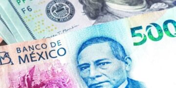 Billetes de peso mexicano y dólares estadounidenses sobre una mesa, con gráfico de tipo de cambio al fondo