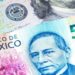 Billetes de peso mexicano y dólares estadounidenses sobre una mesa, con gráfico de tipo de cambio al fondo