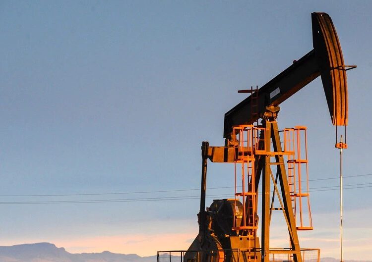 Plataforma petrolera con barriles de crudo apilados al fondo mientras un barco navega por el estrecho de Ormuz