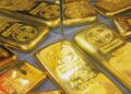 Lingotes de oro apilados sobre una superficie reflejante con gráfico de cotizaciones al fondo