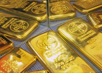 Lingotes de oro apilados sobre una superficie reflejante con gráfico de cotizaciones al fondo