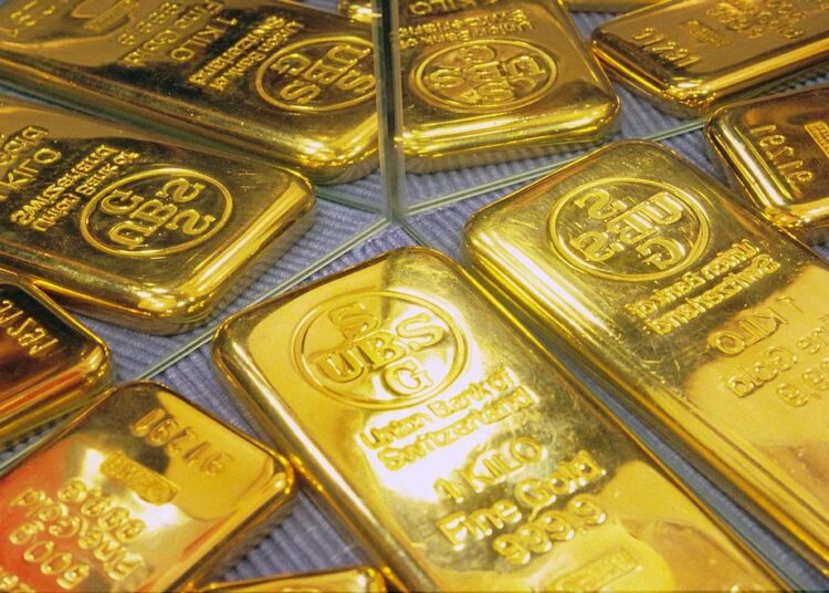 Lingotes de oro apilados sobre una superficie reflejante con gráfico de cotizaciones al fondo