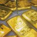Lingotes de oro apilados sobre una superficie reflejante con gráfico de cotizaciones al fondo