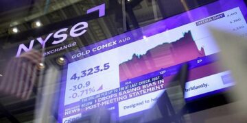 Barras de oro apiladas con cotización en pantalla financiera durante jornada de mercados en agosto de 2026